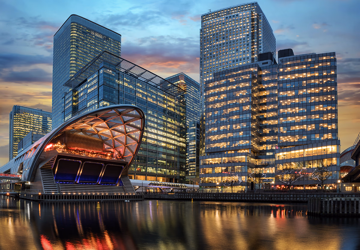 Canary Wharf's skyscrapers lit up at dusk, reflected in the dock